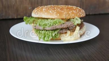 一个大的美味多汁的汉堡，有三层切块、新鲜<strong>生菜叶</strong>和奶酪，放在一个时髦的白色盘子上